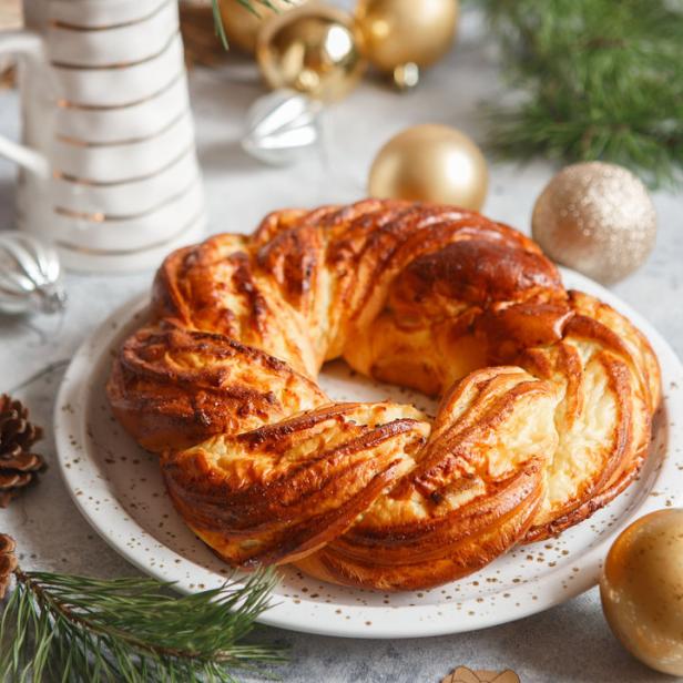 Ein Hefekranz liegt auf einem Teller, umgeben von Weihnachtskugeln und Tannenzweigen.