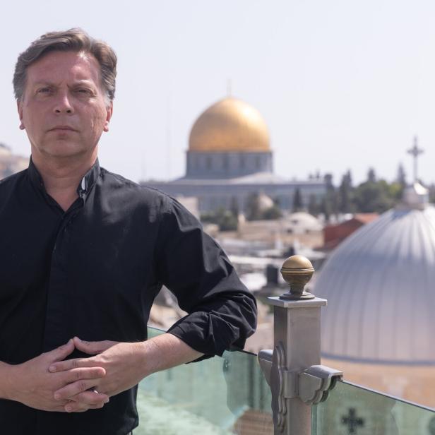 Ein Mann steht auf einer Terrasse mit Blick auf die goldene Kuppel des Felsendoms und eine silberne Kuppel im Hintergrund.