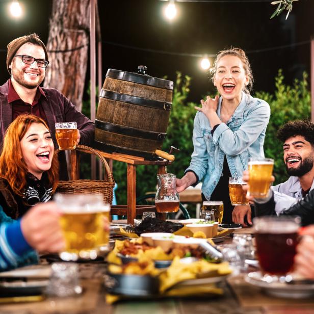 Eine Gruppe junger Leute lacht und trinkt Bier an einem Tisch im Freien.