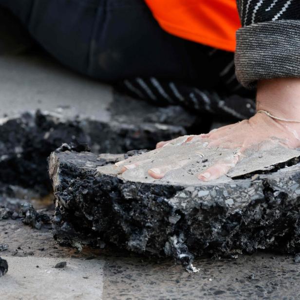 Eine Hand ist mit Beton auf einem Stück herausgebrochener Asphalt festgeklebt.