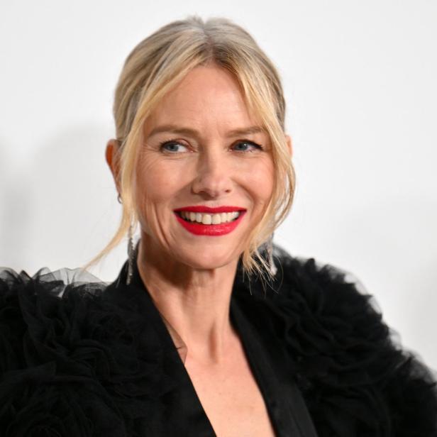 Naomi Watts lächelt in einem schwarzen Kleid.