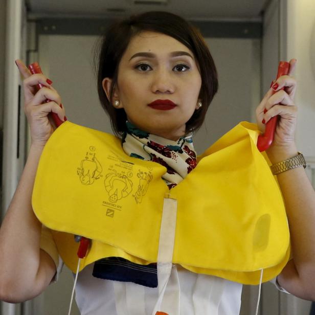 Eine Flugbegleiterin demonstriert die Verwendung einer Schwimmweste im Flugzeug.