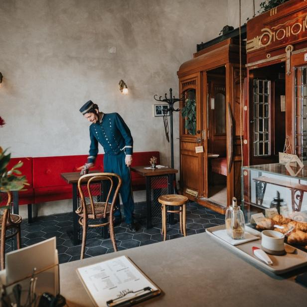 Ein Hotelangestellter in Uniform putzt einen Tisch in einem Café mit Zugabteilen.