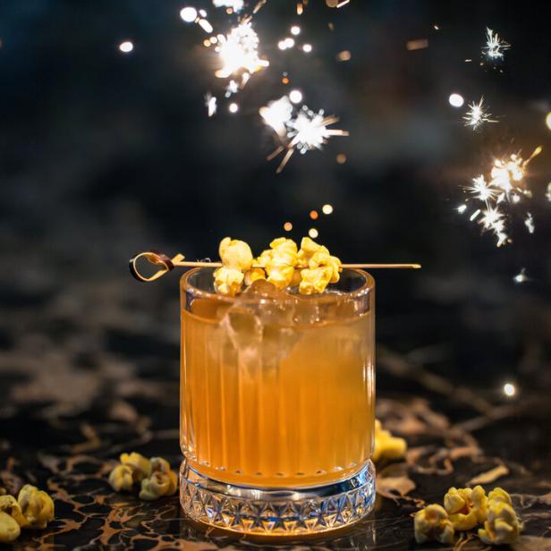 Ein Cocktail mit Popcorn-Garnitur vor einem Hintergrund aus Wunderkerzen.