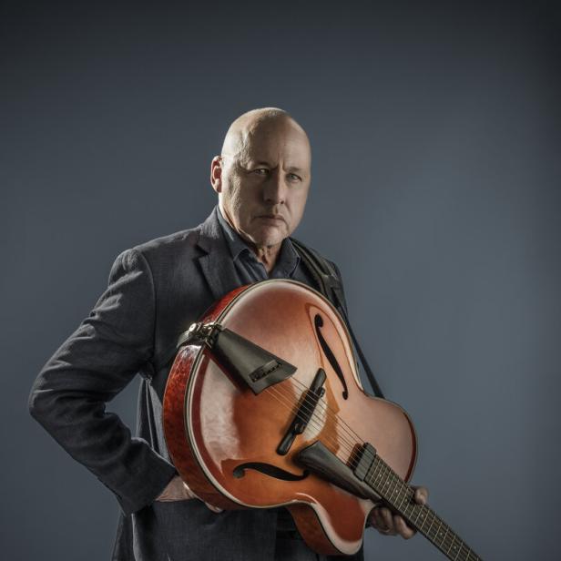 Ein Mann im Anzug hält eine Archtop-Gitarre.