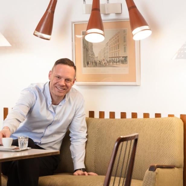 Ein lächelnder Mann sitzt in einem Café und trinkt einen Kaffee.
