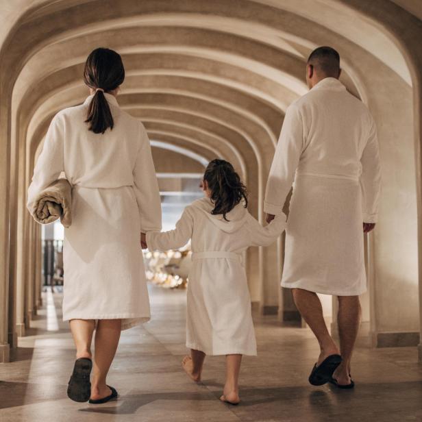 Eine Familie in Bademänteln geht in einem Wellnesshotel einen Flur entlang.