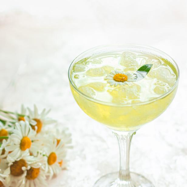 Ein Cocktail mit Eiswürfeln und einer Kamillenblüte als Dekoration.