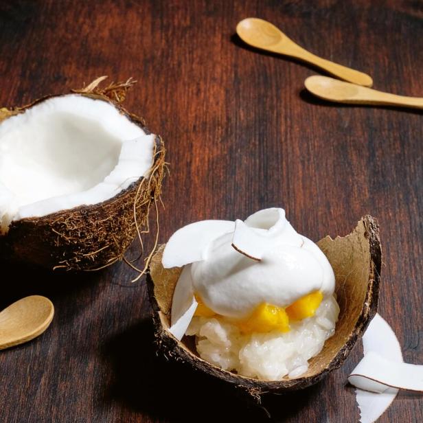 Klebriger Reis mit Mango und Kokosnusscreme, serviert in einer Kokosnussschale.
