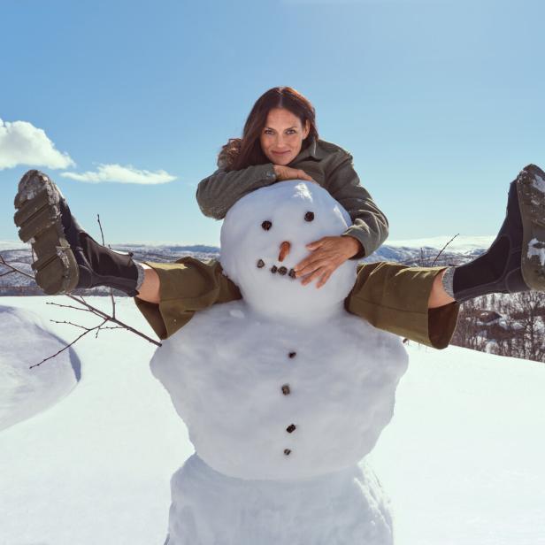 Eine Frau sitzt auf einem Schneemann in einer verschneiten Landschaft.