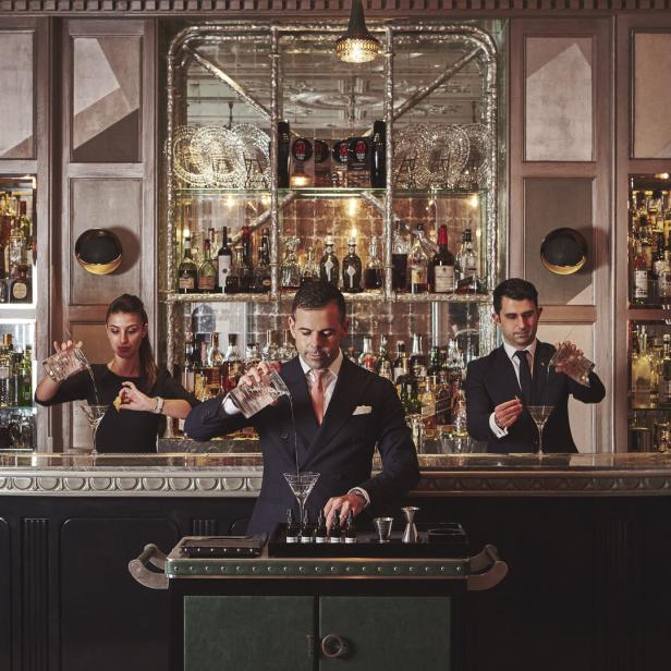 Drei Barkeeper bereiten in einer eleganten Bar Cocktails zu.