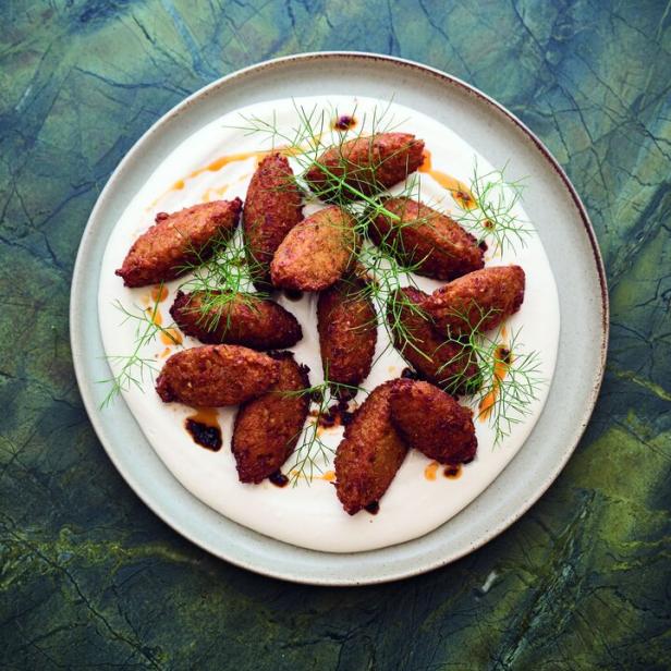 Eine Platte mit Kibbeh auf einer Joghurtbasis, garniert mit Dillspitzen und einem dunklen Balsamico-Dressing.