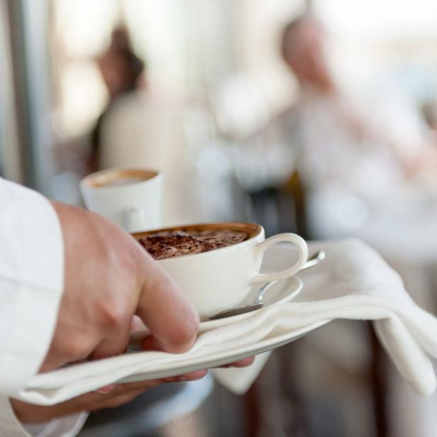 Ein Kellner serviert zwei Tassen Kaffee auf einem Tablett.