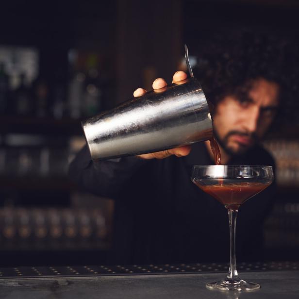 Ein Barkeeper gießt einen Cocktail aus einem Shaker in ein Glas.