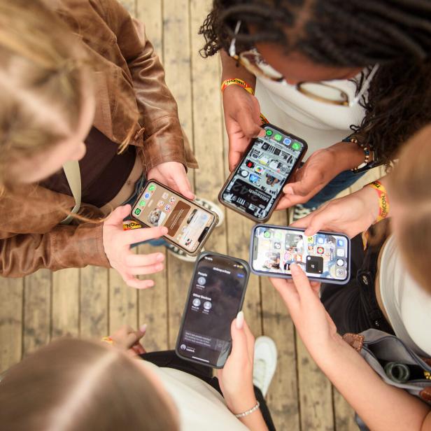 Fünf junge Frauen stehen im Kreis und schauen auf ihre Smartphones.