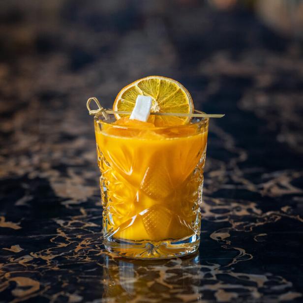 Ein Kürbis-Cocktail, garniert mit einer Orangenscheibe und einem Marshmallow, steht auf einer Bar.