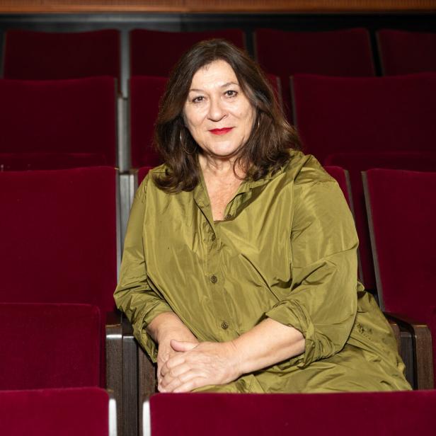 Eine Frau sitzt in einem leeren Theatersaal mit roten Sitzen.