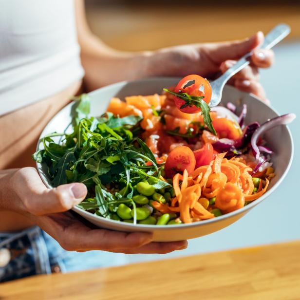 Eine Person hält eine Schüssel mit Salat, Tomaten, Karotten und Edamame.