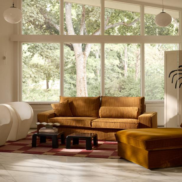 Ein Wohnzimmer mit einem orangefarbenen Sofa, Sesseln und einem großen Fenster mit Blick auf einen Garten.
