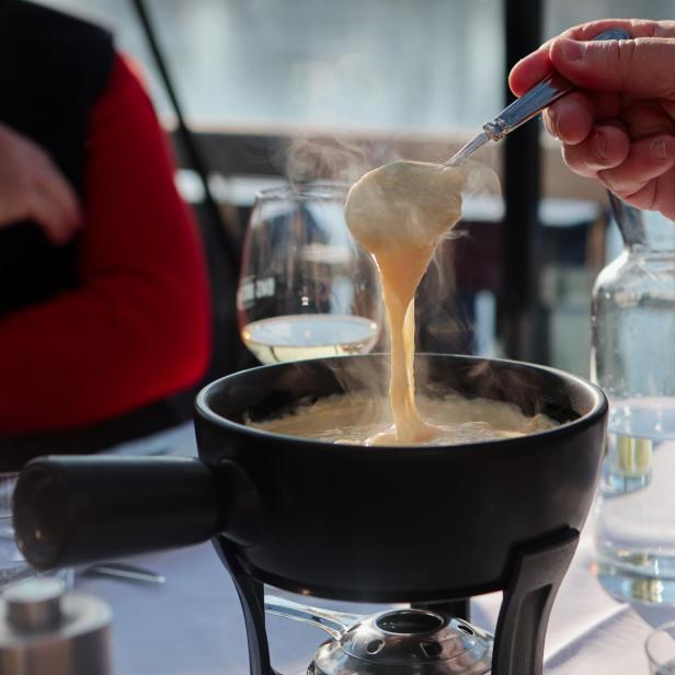 Eine Person hebt mit einem Löffel dampfendes Käsefondue aus einem Topf.