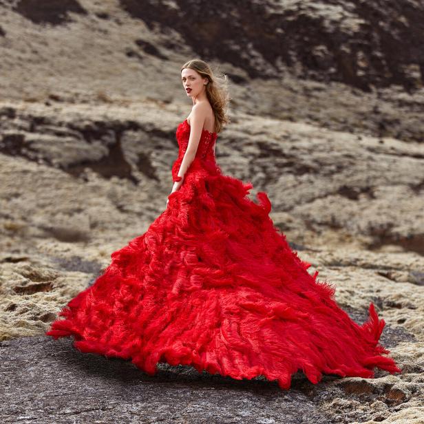Eine Frau in einem roten Kleid steht in einer kargen Landschaft.