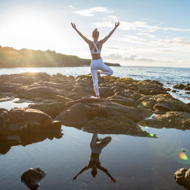 Eine Frau macht Yoga auf einem Felsen am Meer bei Sonnenaufgang.