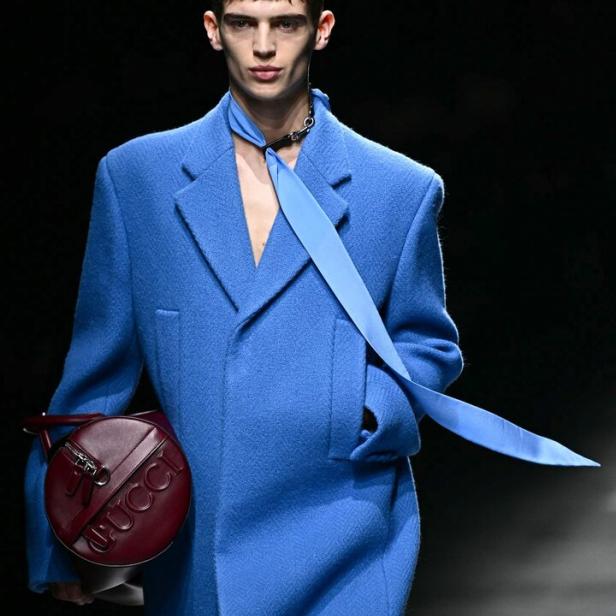 Ein Mann in einem blauen Mantel mit einer runden Gucci-Tasche auf dem Laufsteg.