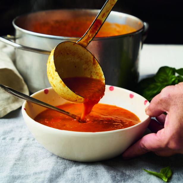 Eine Person gießt mit einer Schöpfkelle Tomatensuppe in eine Schüssel.