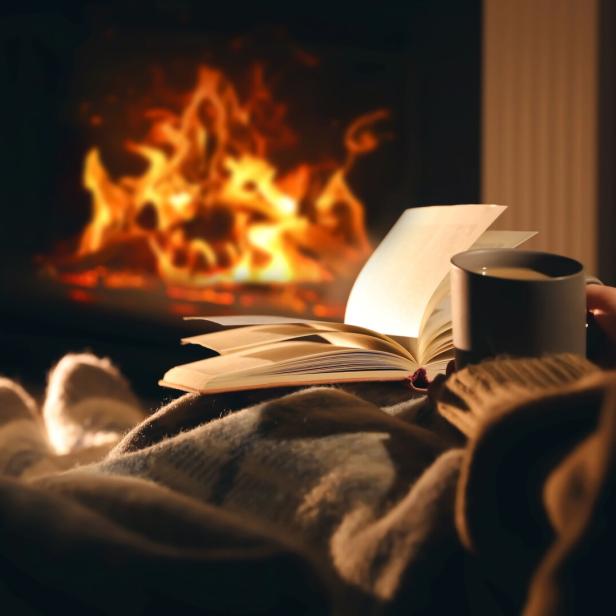 Eine Person liest ein Buch und trinkt eine Tasse Kaffee vor einem Kamin.