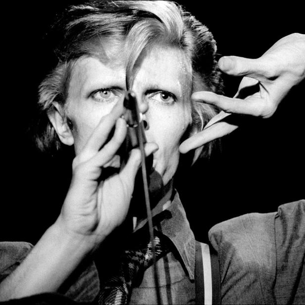 David Bowie singt in einem dunklen Raum mit einem Mikrofon vor dem Gesicht.