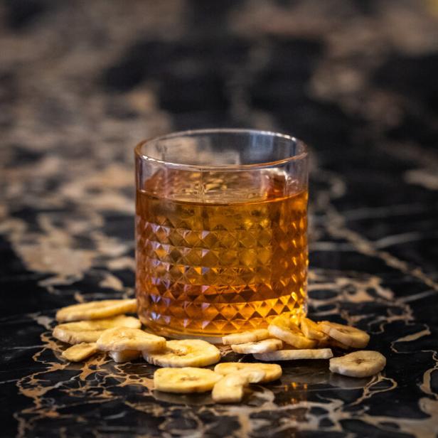 Ein Cocktail, garniert mit Bananenchips, steht auf einem Marmortisch.