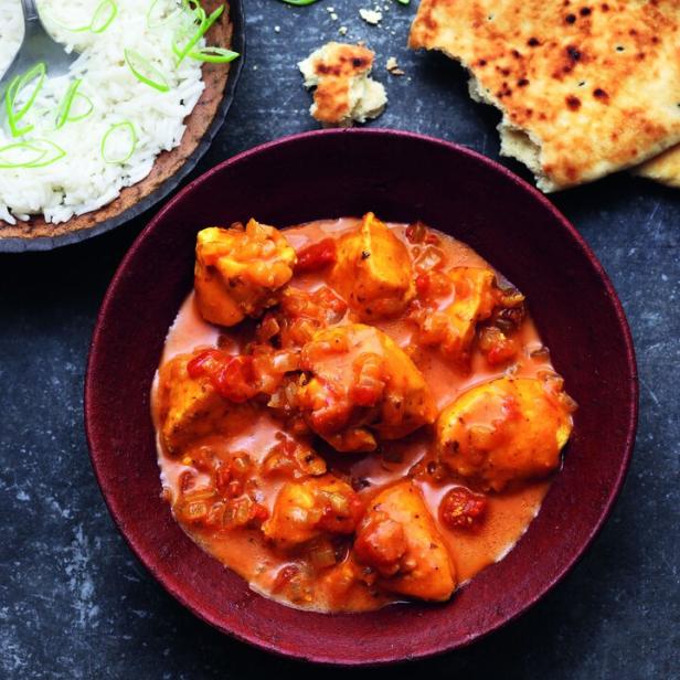 Ein Teller mit Hühnchen-Curry, serviert mit Reis und Naan-Brot.