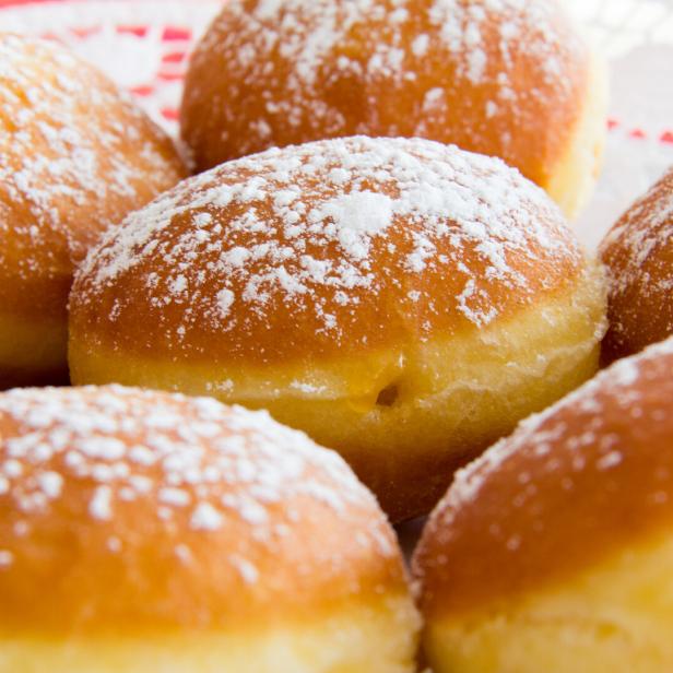 Mehrere Krapfen mit Puderzucker auf einem Teller.