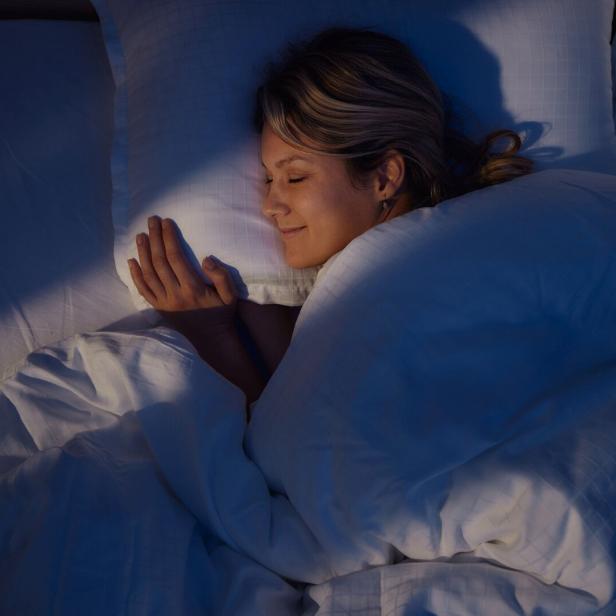 Eine Frau schläft friedlich in ihrem Bett unter einer weißen Decke.