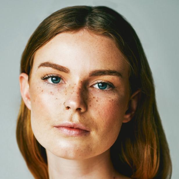 Porträt einer jungen Frau mit Sommersprossen und hellblauen Augen.