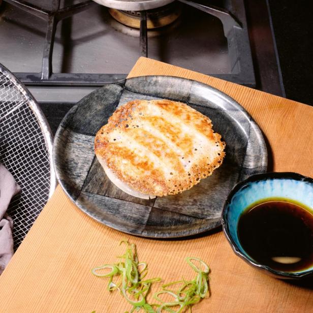 Zwei Teller mit gebratenen Gyoza, serviert mit Sojasauce und Frühlingszwiebeln.
