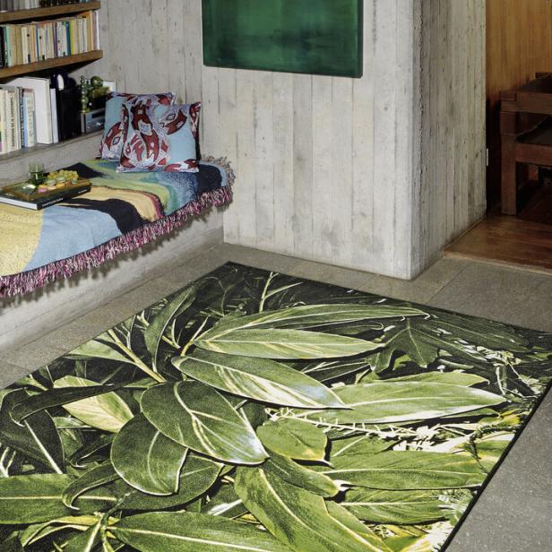Ein Raum mit Betonwänden, einem grünen Gemälde und einem Teppich mit Blattmuster.