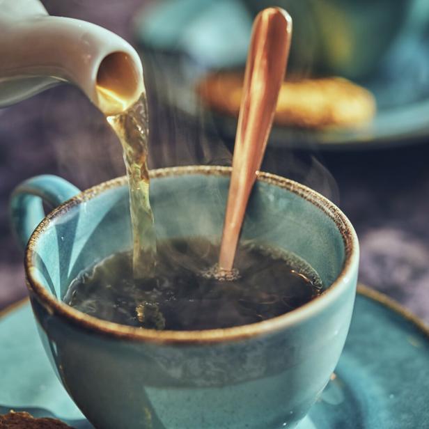 Tee wird in eine hellblaue Tasse mit Untertasse gegossen.