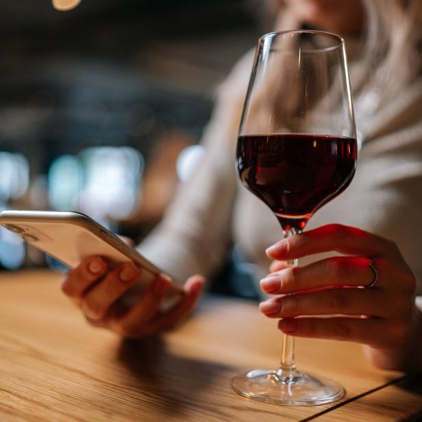 Eine Frau hält ein Glas Rotwein und ein Smartphone in der Hand.