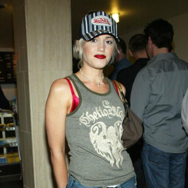 Gwen Stefani trägt ein Tanktop, Baggy Jeans, rote Schuhe und eine Kappe.