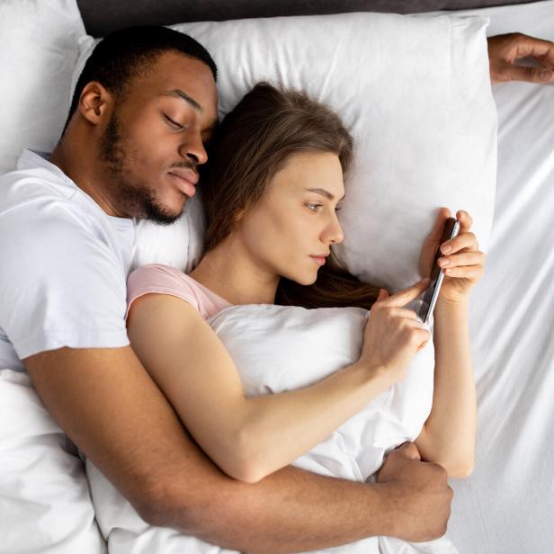 Mann und Frau liegen im Bett, die Frau benutzt ihr Handy.