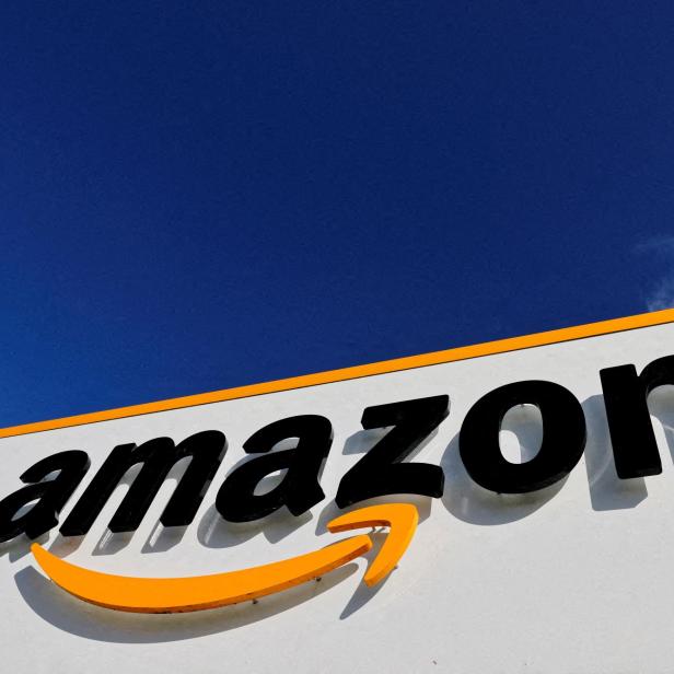 Das Amazon-Logo mit gelbem Pfeil ist auf einer weißen Wand vor blauem Himmel zu sehen.