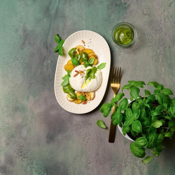 Burrata mit gerösteten Kartoffeln, Paprika und Basilikumpesto auf einem Teller.