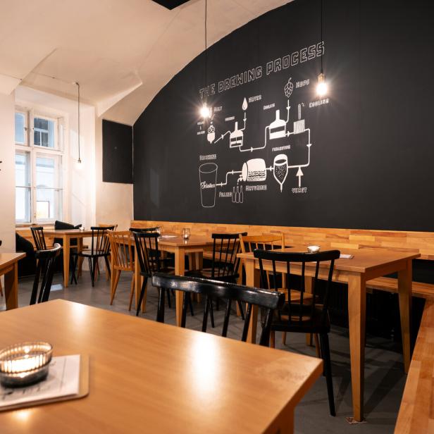 Innenansicht eines Restaurants mit Holztischen und einer Wandzeichnung des Brauprozesses.