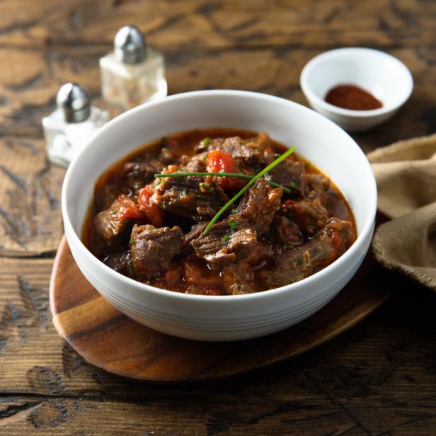Rindfleischgulasch in einer Schüssel auf einem Holztisch.