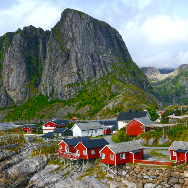 Rote Holzhäuser in einem Fischerdorf vor einer beeindruckenden Bergkulisse in Norwegen.