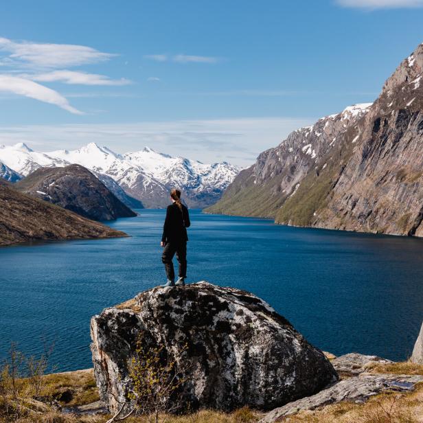 Eine Person steht auf einem Felsen und blickt auf einen See und schneebedeckte Berge.