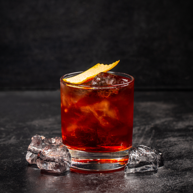 Ein Cocktail mit Eiswürfeln und einer Orangenzeste auf einem dunklen Untergrund.