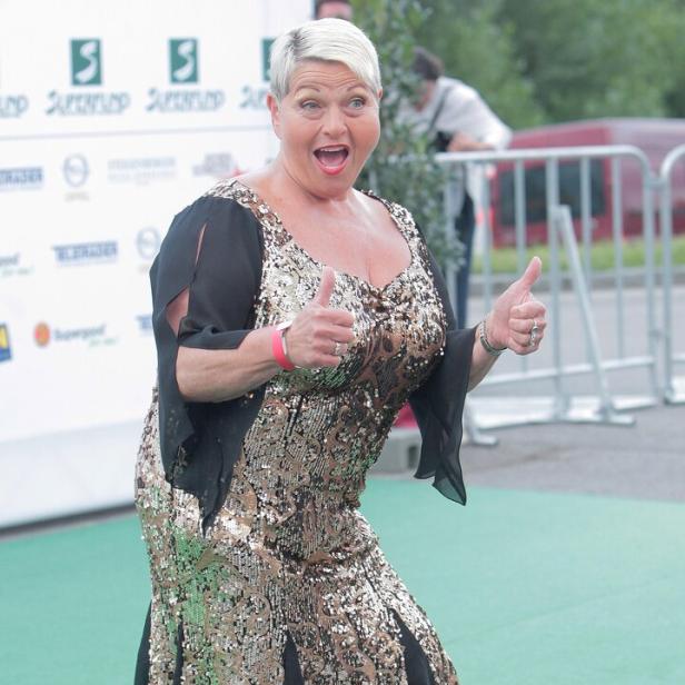 Eine Frau im goldenen Paillettenkleid gibt zwei Daumen hoch.