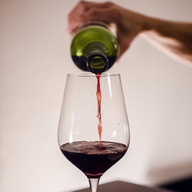 Person schenkt Rotwein aus Flasche in Glas ein.